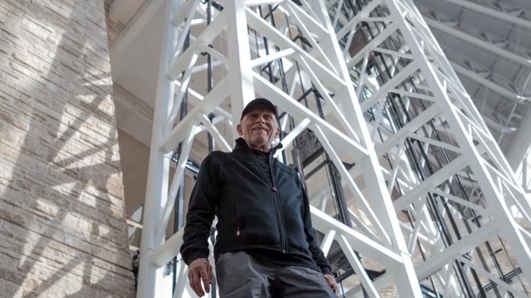 Antoine Predock, the architect of the Museum, is pictured inside the Museum from a low angle with white beams rising above him.