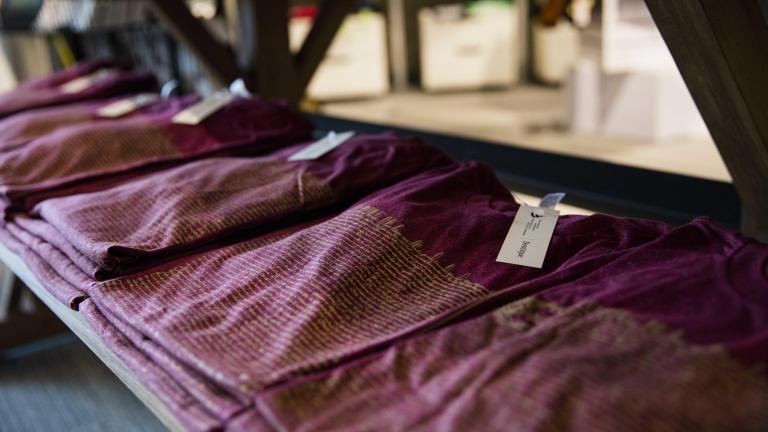 Stacks of three or four folded burgundy t-shirts lay on a wooden table.