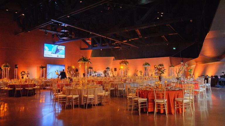A large room with high ceilings, filled with round tables that have formal table settings. 