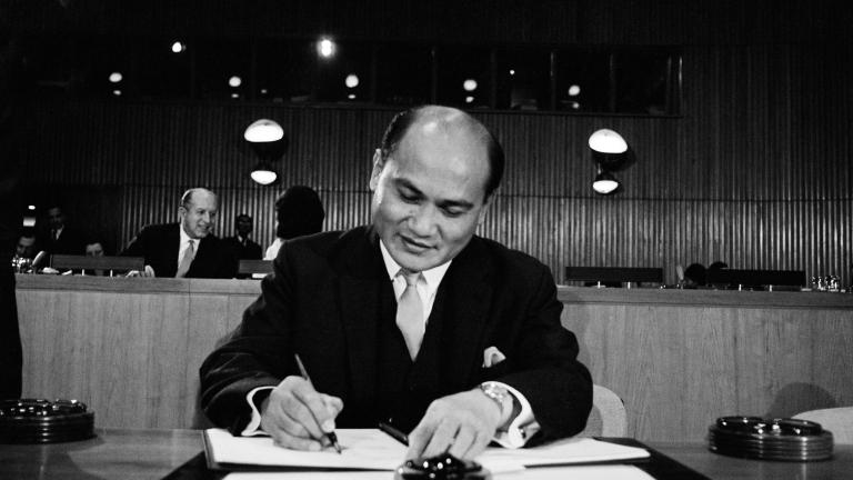 A man wearing a suit signs a document.