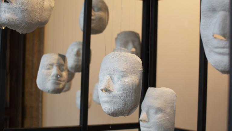 Several white plaster faces hang from strings, inside a cage.
