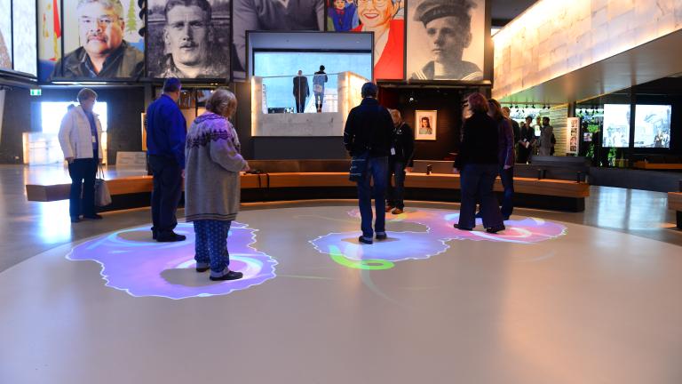 A group of people are standing within part of a white circle. Blue and purple lights are projected onto the floor surrounding each person.