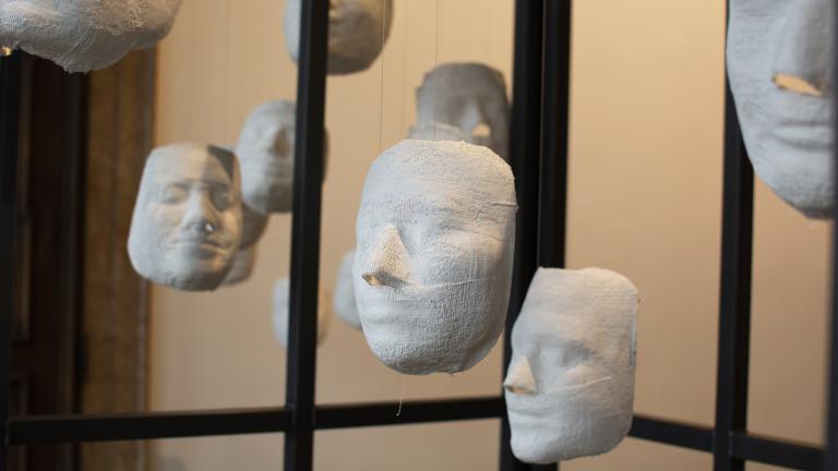 Several white plaster faces hang from strings, inside a cage.