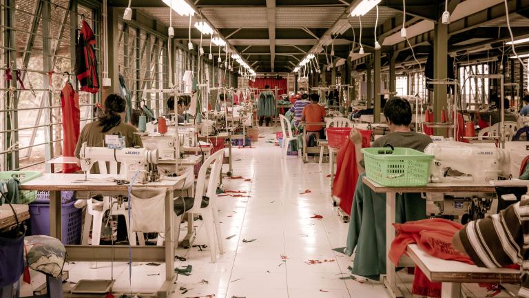 Garment workers sit at desks with sewing machines in a warehouse.