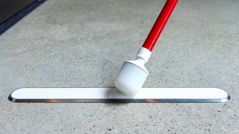 The end of a cane touches a raised strip attached to the floor.