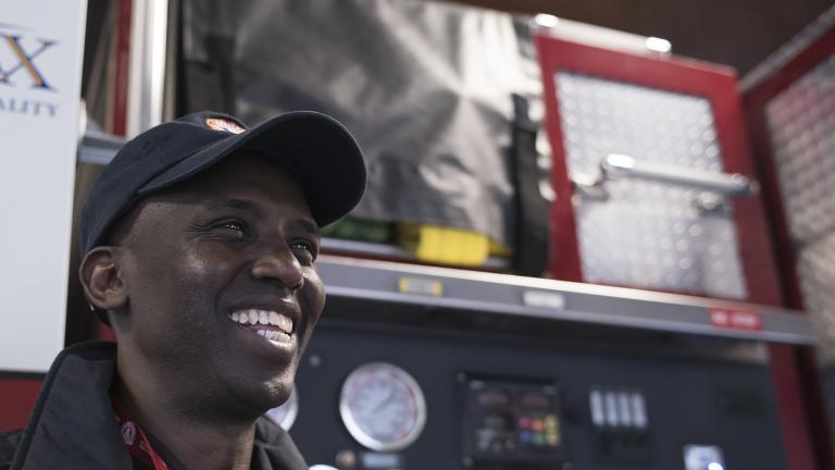 A smiling man stands in front of a fire truck.
