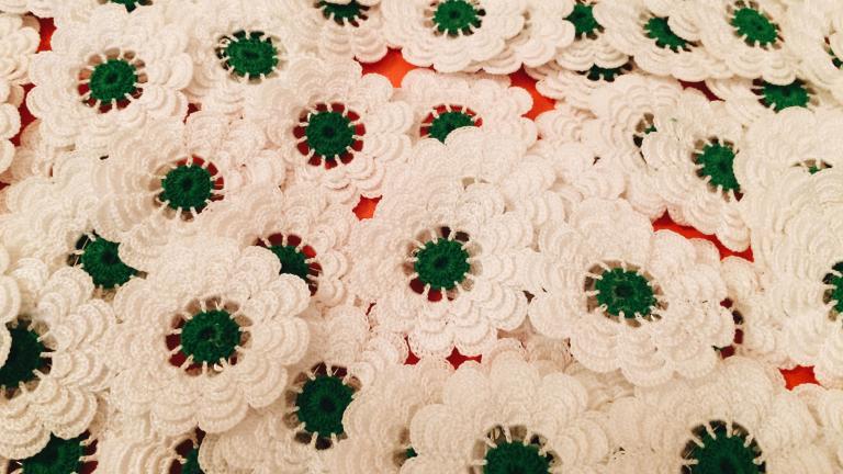 A bunch of knit white flowers with green pistils. Partially obscured.