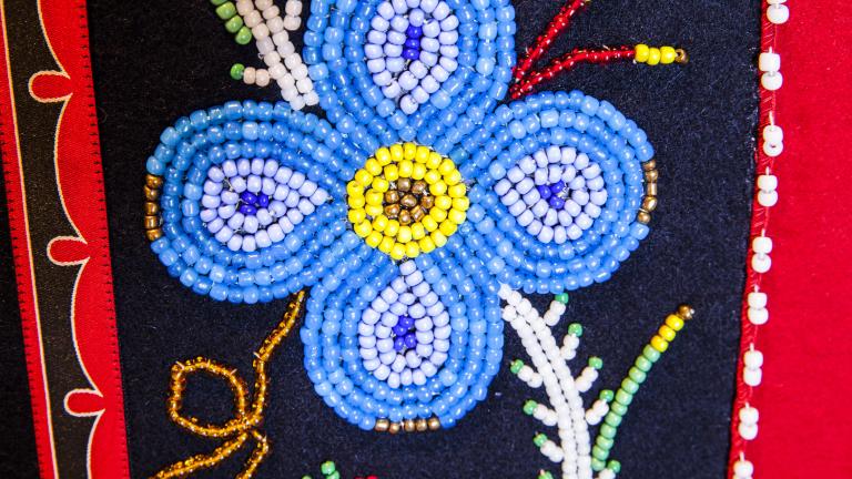 A blue beaded flower on a black and red background. Partially obscured.