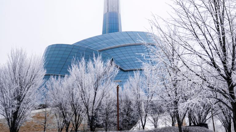 An unusual building surrounded by a glass "cloud" and topped by a tower. It is surrounded by snow and bare trees. Partially obscured.