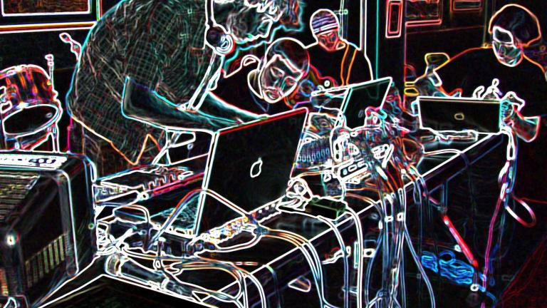 Four people around a table covered in computers and electronic music equipment. The photo has been altered so that the background is black and the elements of the photo are outlined in multi-coloured neon. Partially obscured.
