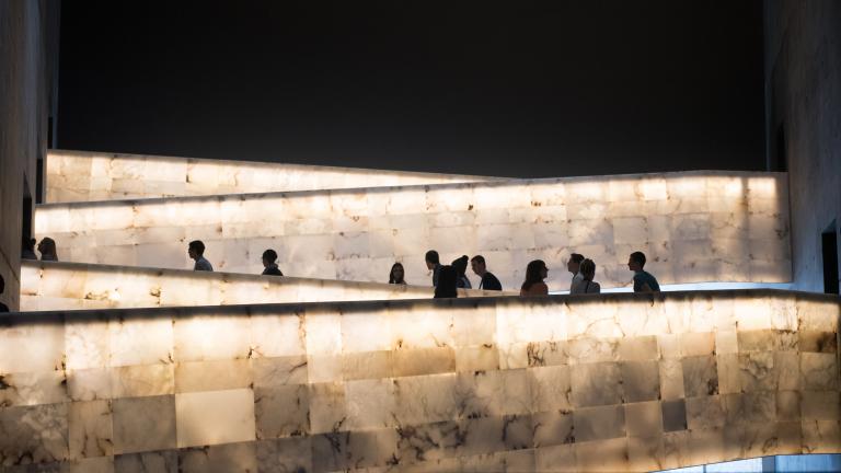 A group of people traveling up the Museum’s lighted alabaster ramps. Partially obscured.