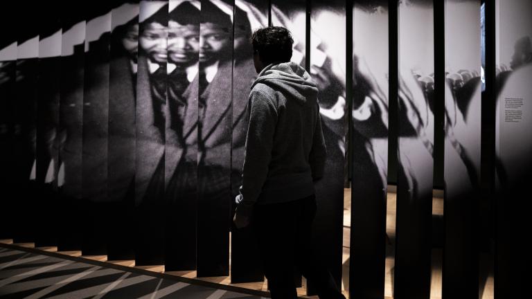 A person walks in front of a large photograph of Nelson Mandela. Partially obscured.