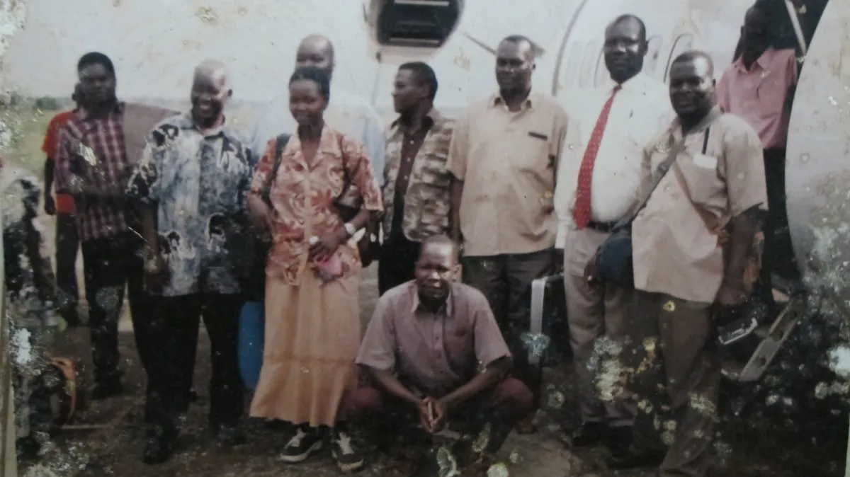 A group of nine people are standing in front of a white background in an outdoor setting, posed for the camera.