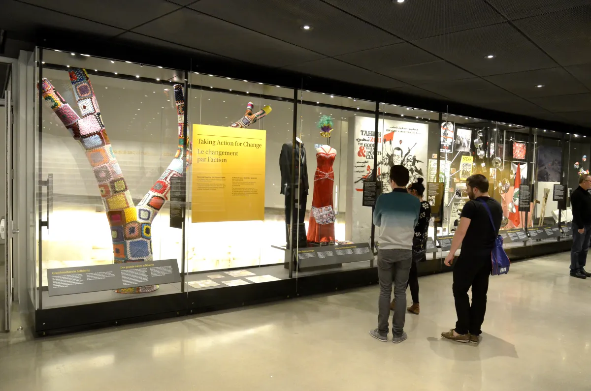 Museum visitors observe a glass display containing images and objects.