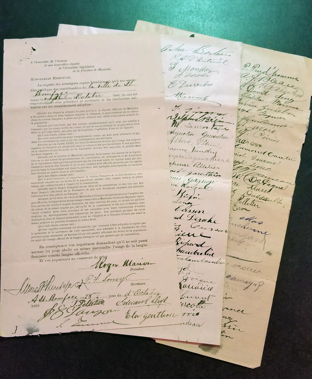 A close-up of an original French-language petition with two pages of signatures fanned out behind it.