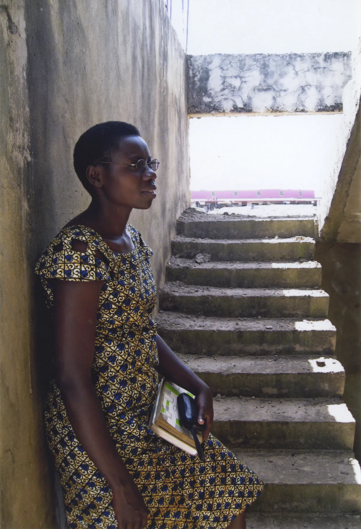 A woman holding a book leans against a wall.