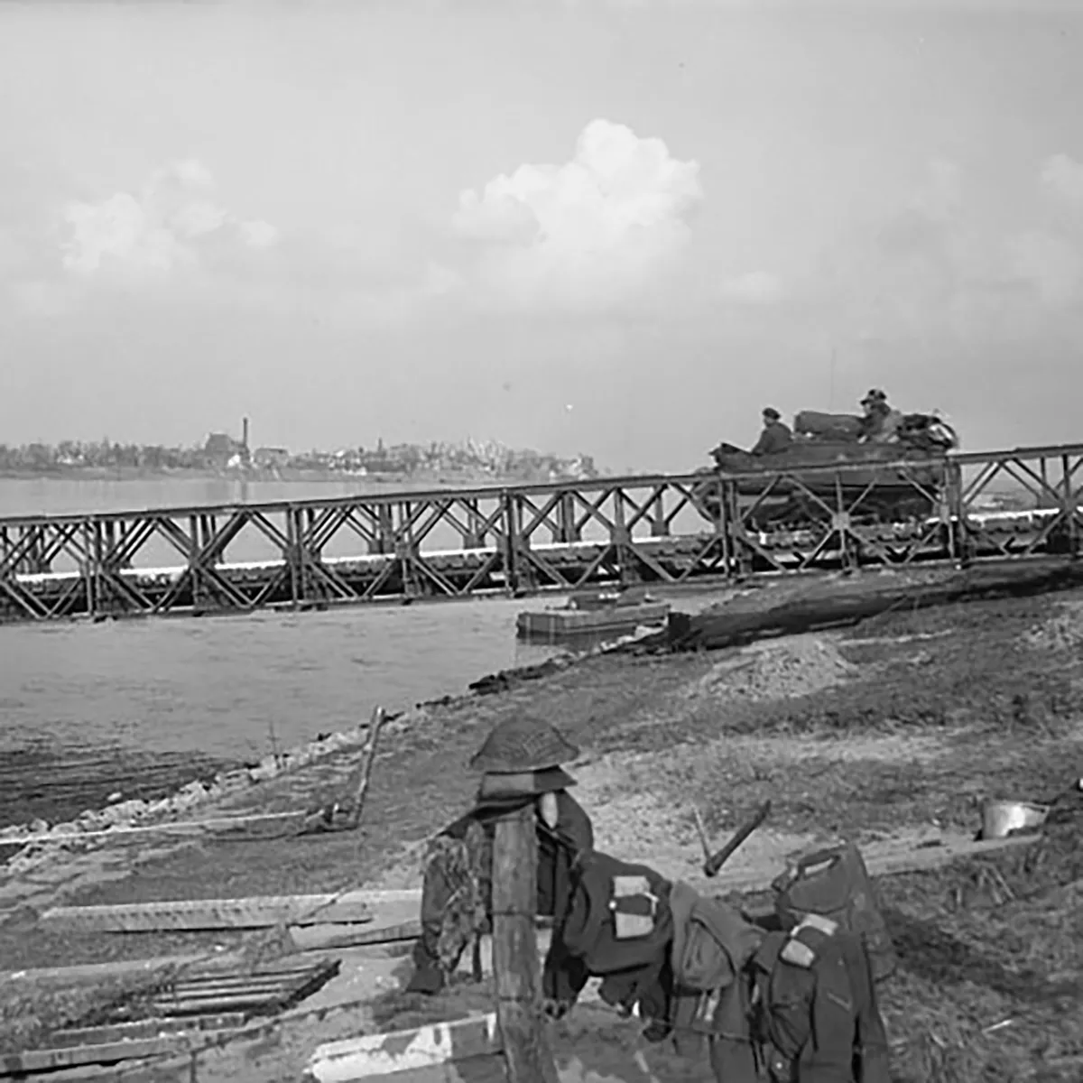 A group of armed soldiers watch a tank drive past.