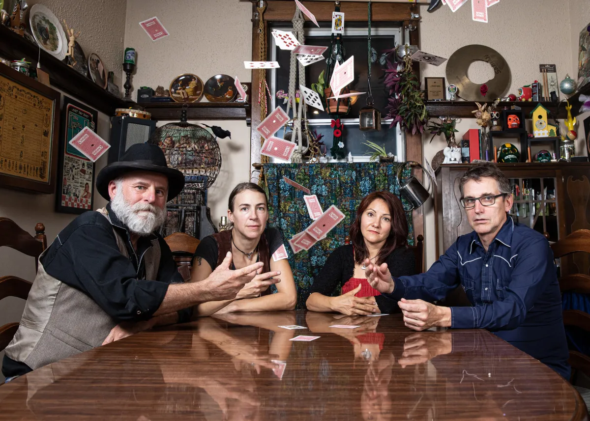 Four people sitting at a table throwing a deck of cards up in the air.