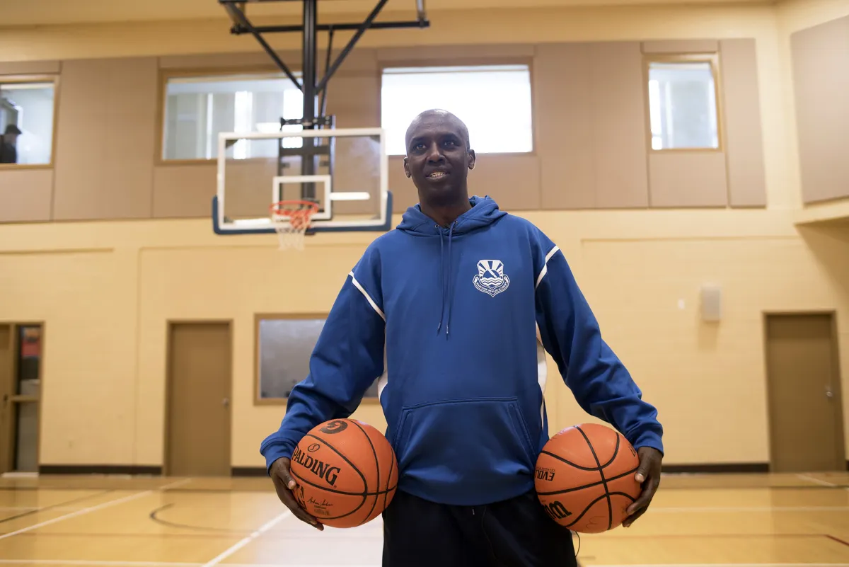 A man stands in a basketball court holding two basketballs. 