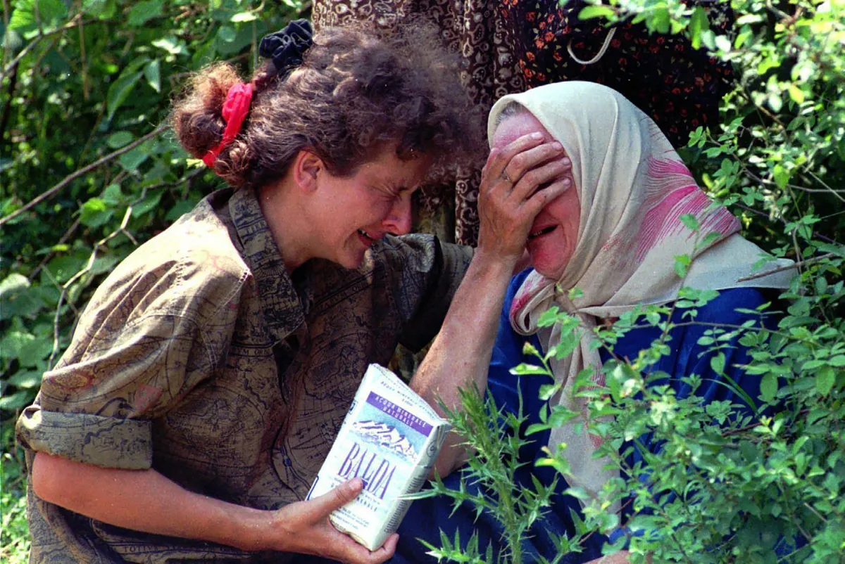 A woman holds another woman who covers her face with her hand. Both are weeping.