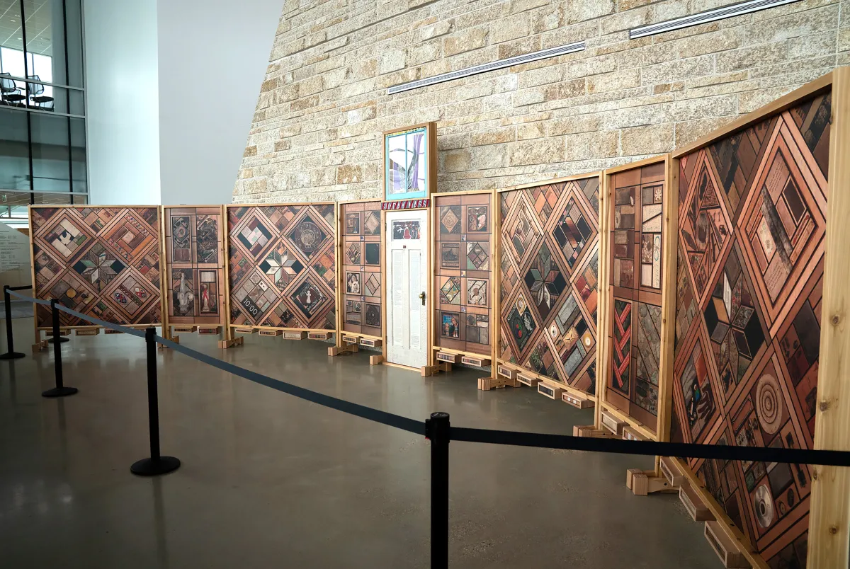 Right view of a structure of vertical wood panels covered in patterns of images, with a white wooden door at the centre.