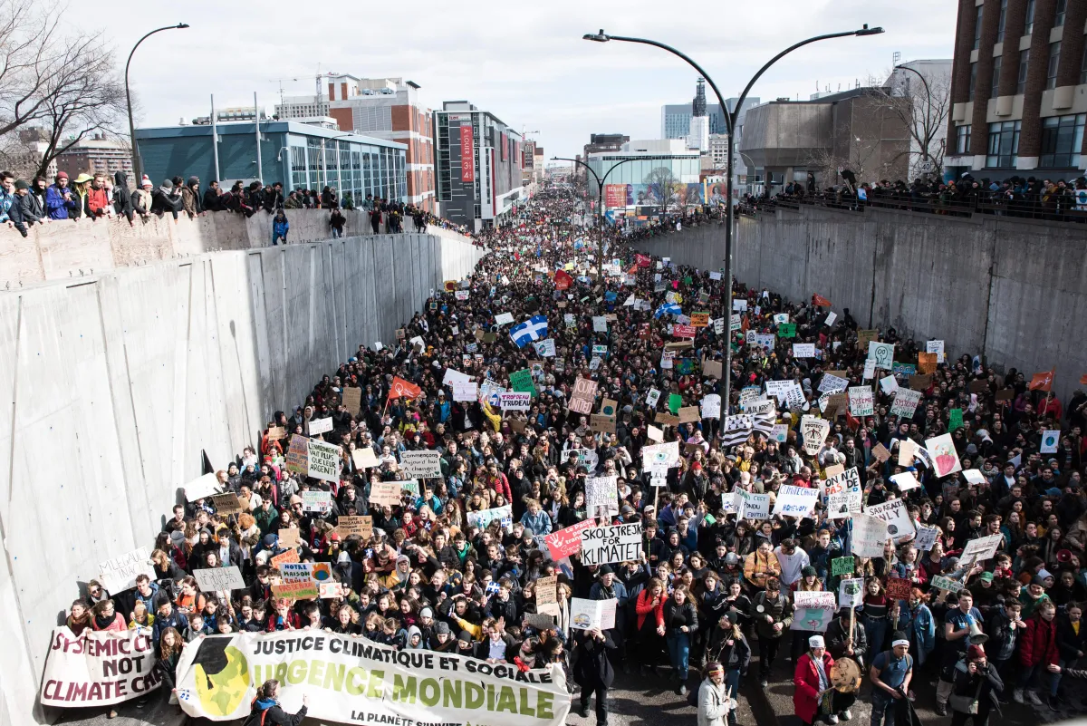 Thousands of people are holding protest signs and banners while marching in a street.
