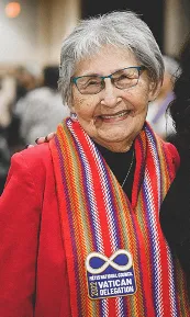 Une femme aux cheveux gris courts porte un foulard multicolore sur les épaules et un blazer rouge.