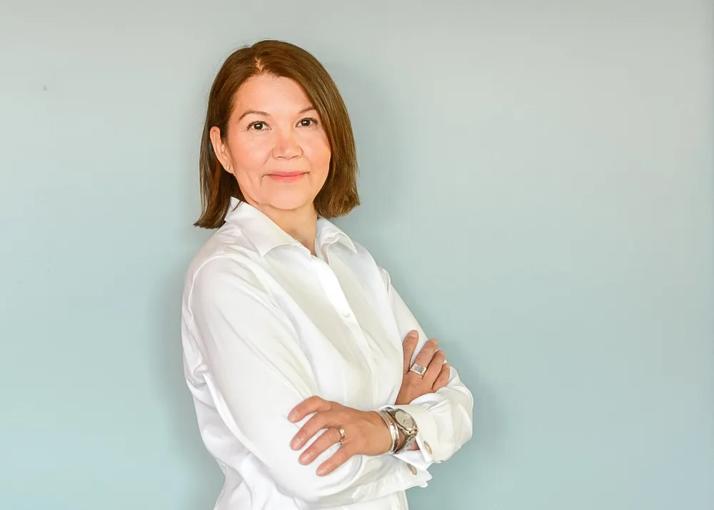 A woman with a brown straight shoulder length hair and a white blouse.
