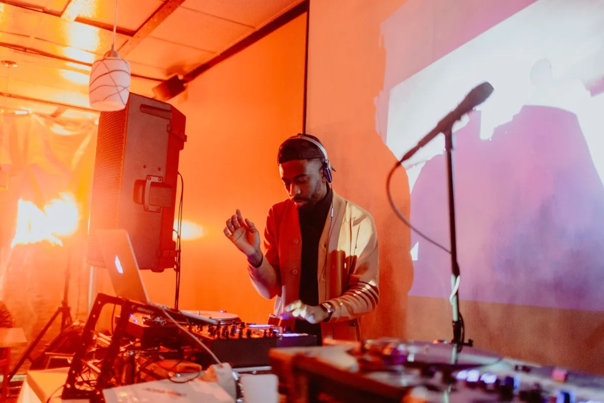 Zuki, un jeune Noir portant un blazer doré, travaille comme platiniste entouré de matériel audio.