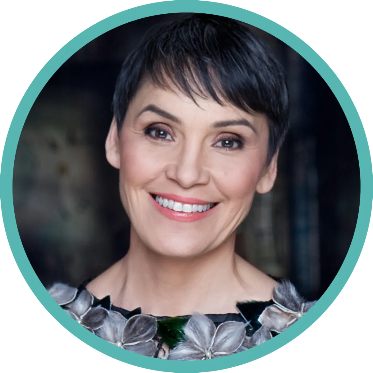 A woman with short dark hair and a blouse with a collar of flowers smiles.