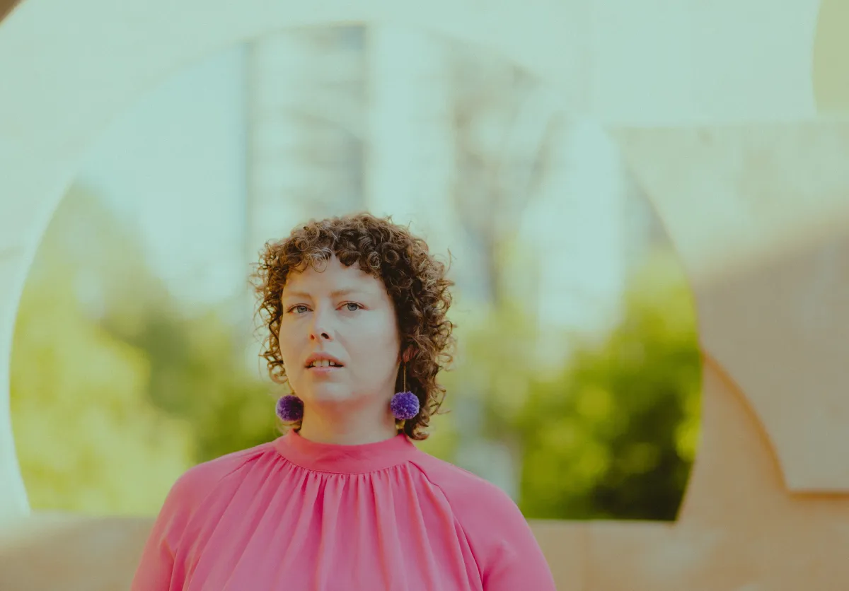 A woman in a pink shirt with a green-leafy background.