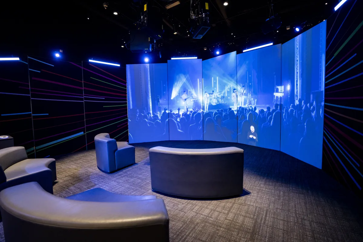 Curved couches face a curved theatre-style screen that displays a concert.