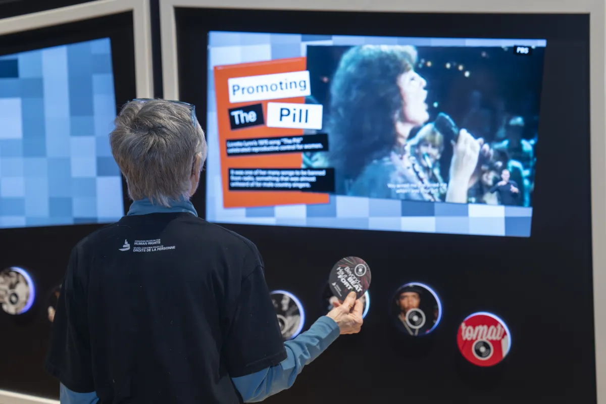 A visitor uses a disc containing RFID technology to interact with a screen showing a female singer and text. The larger title reads: Promoting the pill.