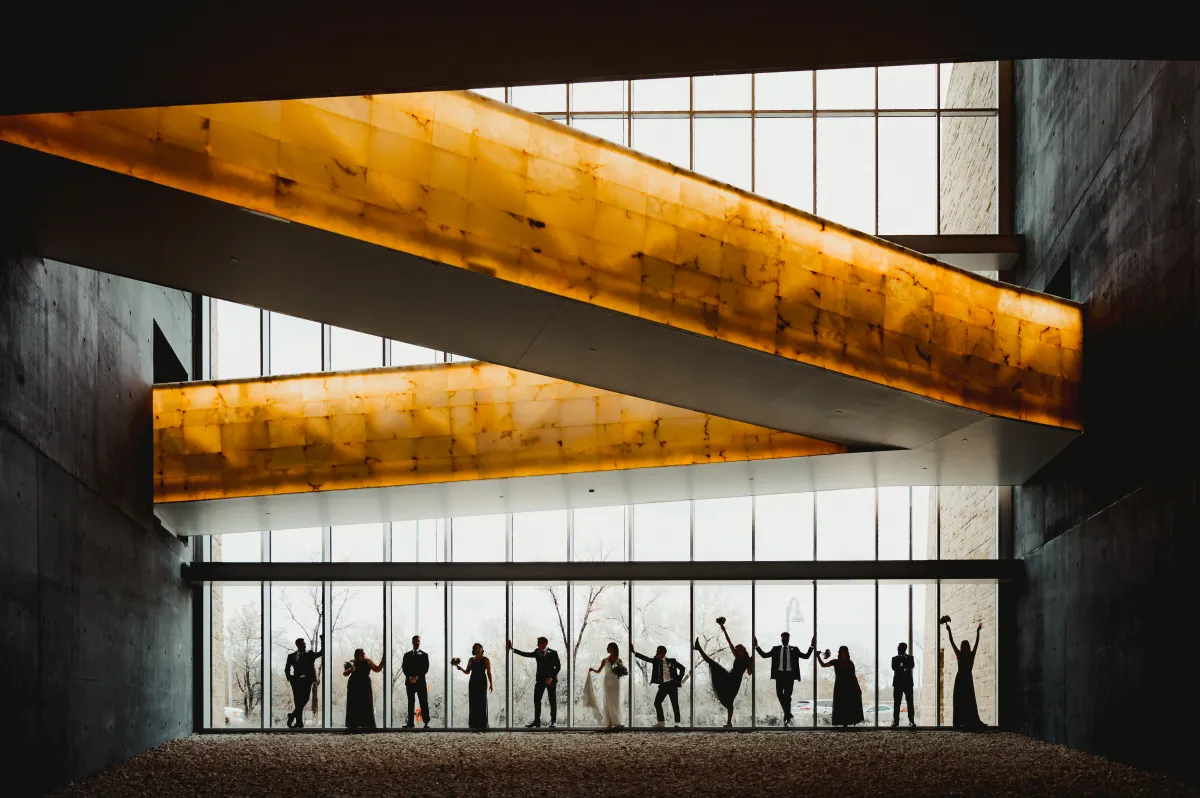 Twelve people are standing in front of a really high window, doing funny poses.