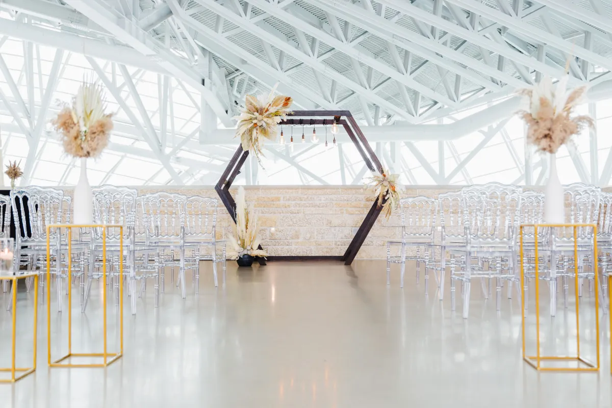 A wedding ceremony set-up with clear chairs and an arch with flowers on it.