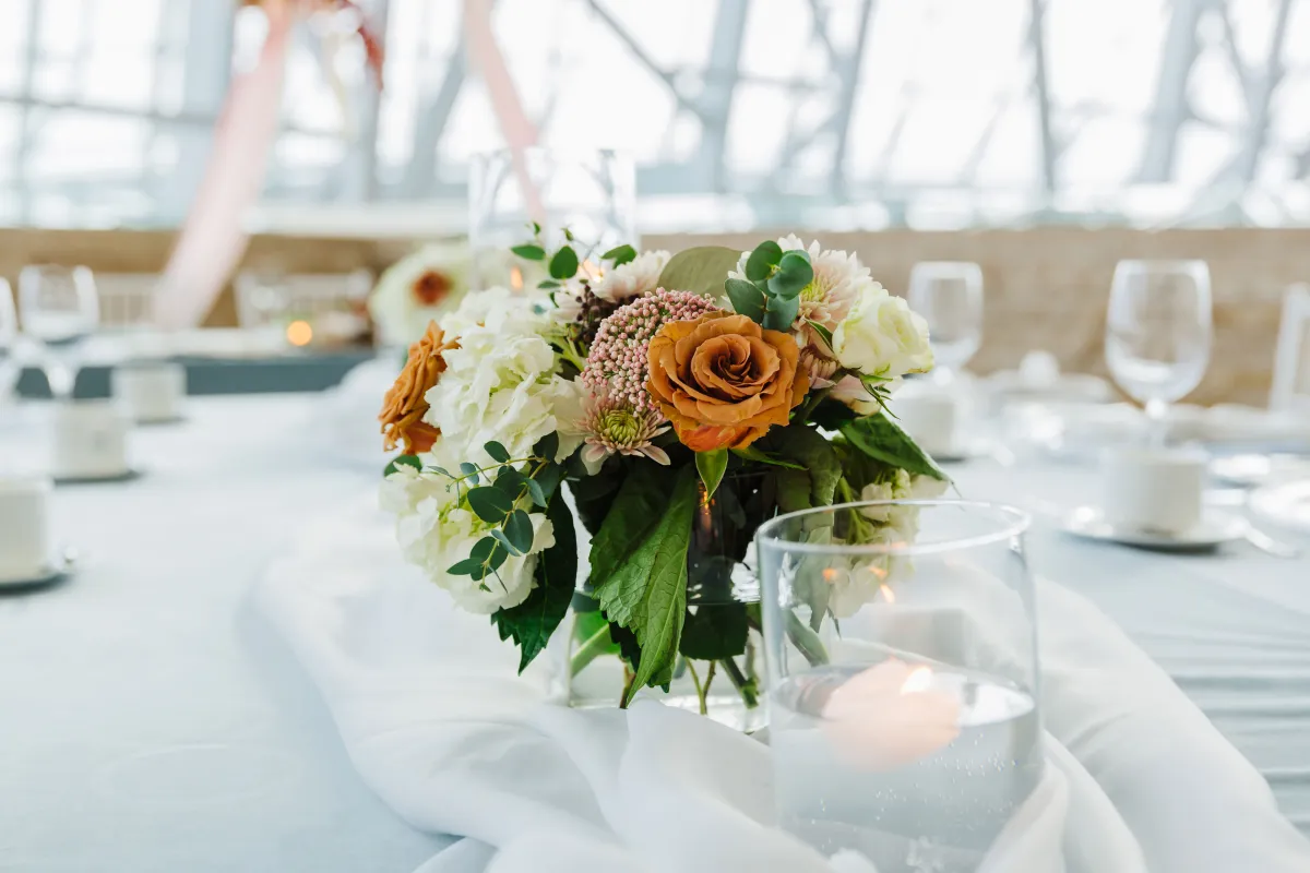 Green, white and orange floral centre piece with a dinner table set in the background.