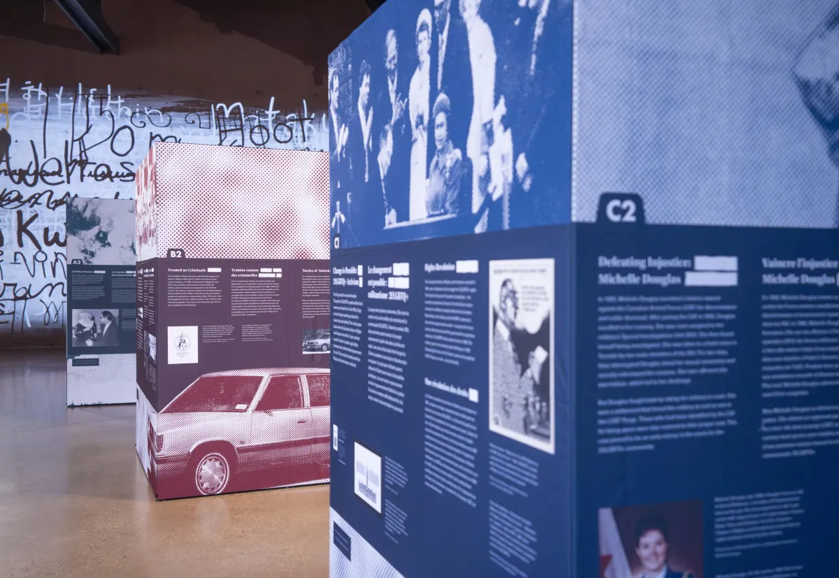 Three large cubes, taller than a person and arranged in a line from front to back, are covered with images and text. These cubes are the pop-up exhibit Love in a Dangerous Time.