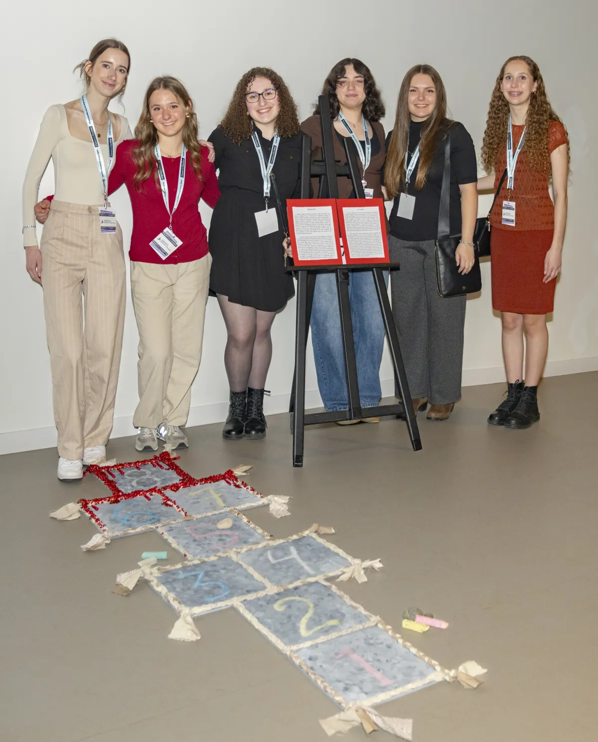 A group of girls stand behind a game of hopscotch. The last few squares have red on them, resembling blood.