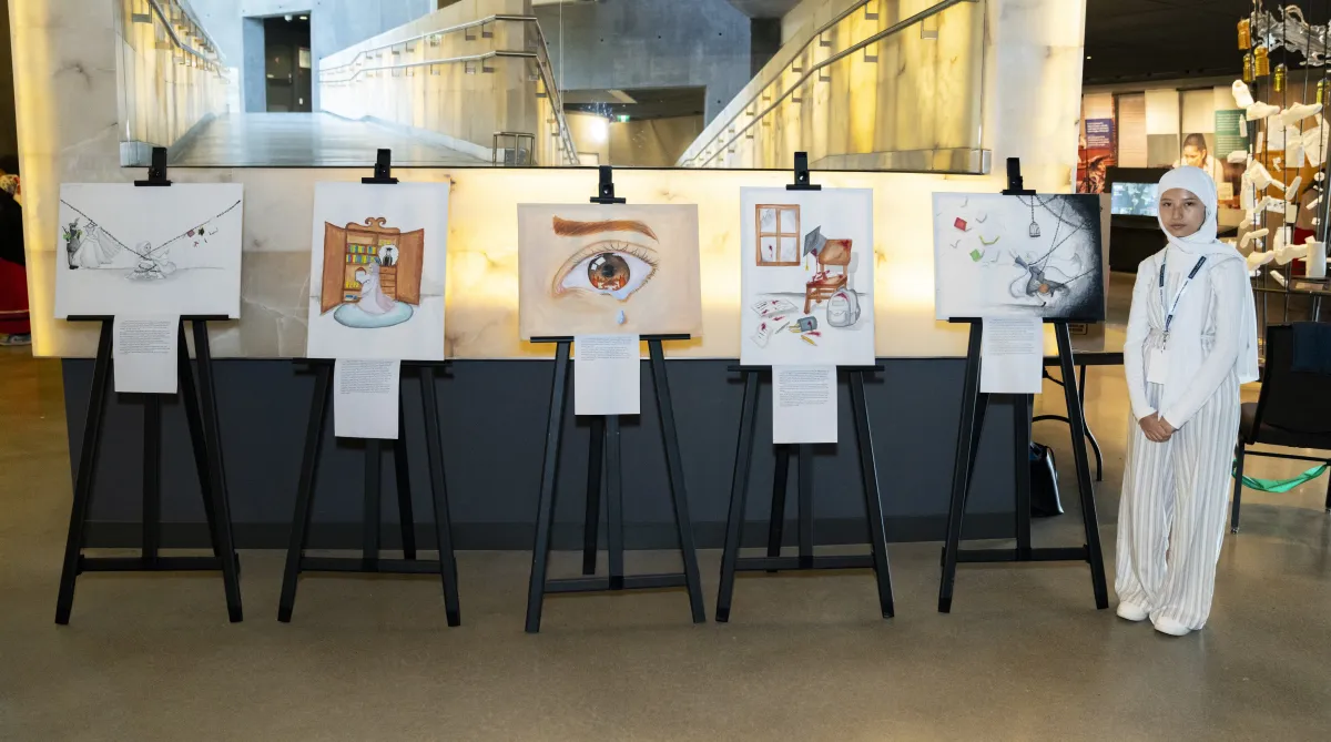 A student standing next to 5 easels that display their original artwork. 