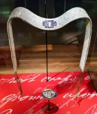 A white-and-blue belt made of shells is displayed on a stand.