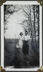  A young woman and a young man pose in a field with trees in the background.