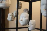 Several white plaster faces hang from strings, inside a cage.