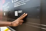 A hand touches braille letters on a museum exhibit.