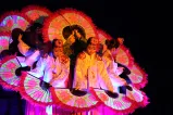 Korean dancers holding large, flower-patterned fans are grouped together so their fans form a circle.