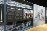 A large exhibit panel on the left features the words “A Clash of Values: Colonization in Early Canada” and a colourful painting. On the right, there is a large black-and-white photograph of people parading in single file in 1940s women’s swimsuits.