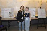 Two students standing in front of a table and an easel that are displaying presentations on poster boards. 