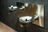 Two water fountains jut out of a wall. They are located side-by-side, but one fountain is set lower than the other.