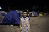 A teenage boy stands in front of tents in a parking lot at night.