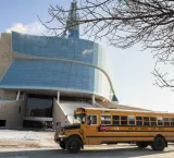 A yellow school bus is parked in front of the Museum. 