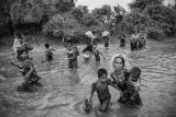 A group of Rohingya women and children carry their belongings as they wade across a canal filled with two to three feet of water.